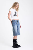 Mid blue denim longline jorts with no waistband and silver piercing hardware detail, worn by model
