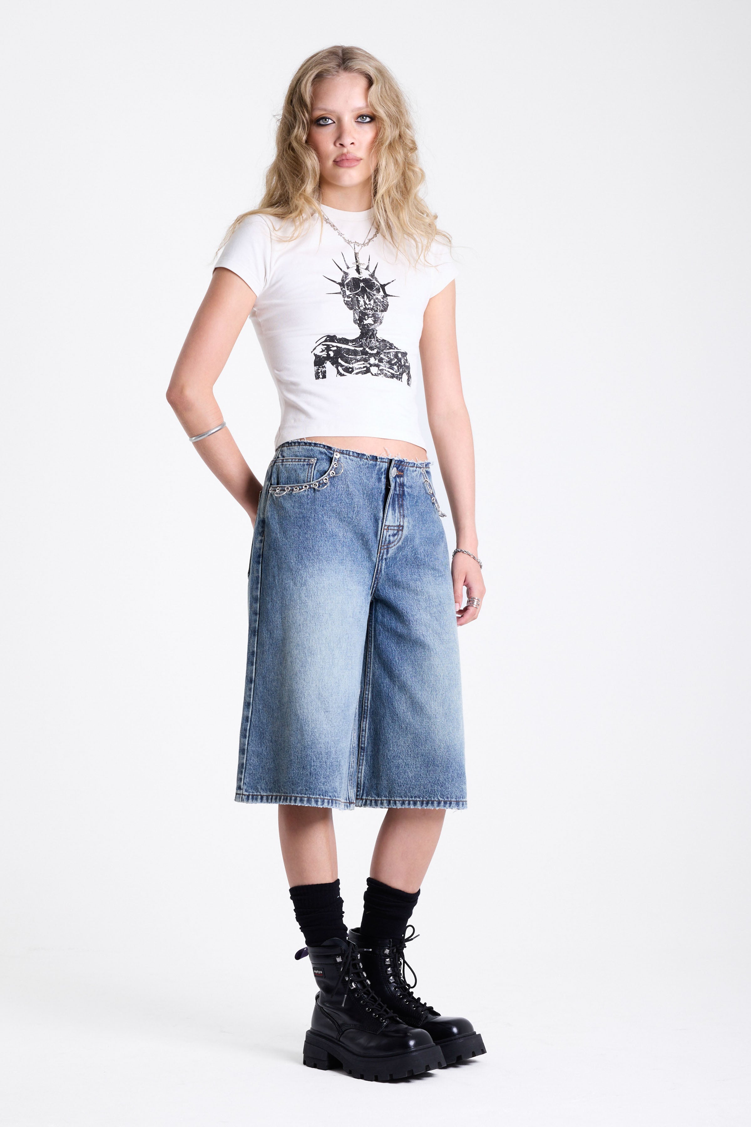 Mid blue denim longline jorts with no waistband and silver piercing hardware detail, worn by model