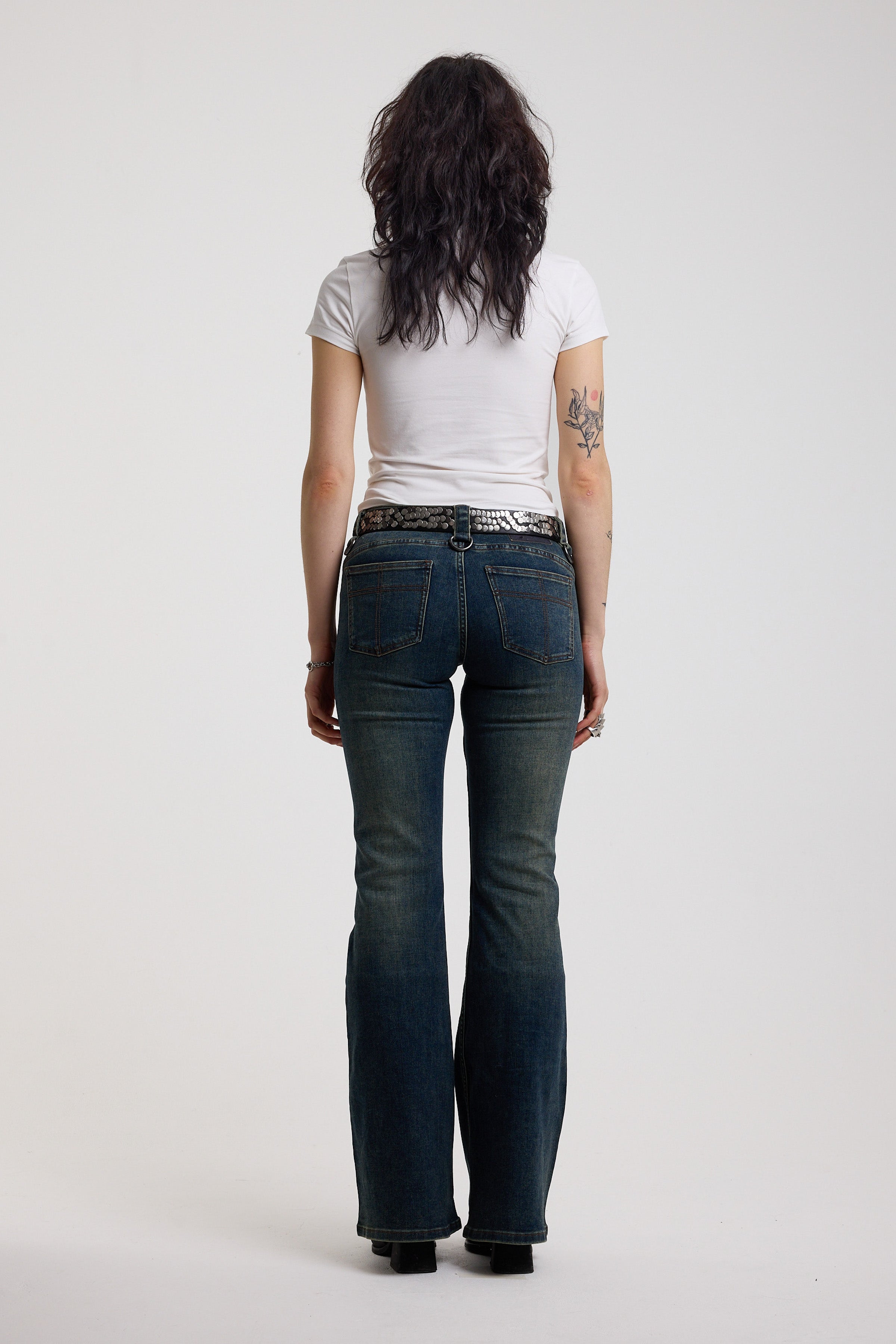 Back of dark blue flare bootcut jeans with silver D-ring hardware detail, worn by model