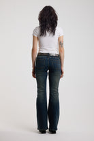 Back of dark blue flare bootcut jeans with silver D-ring hardware detail, worn by model