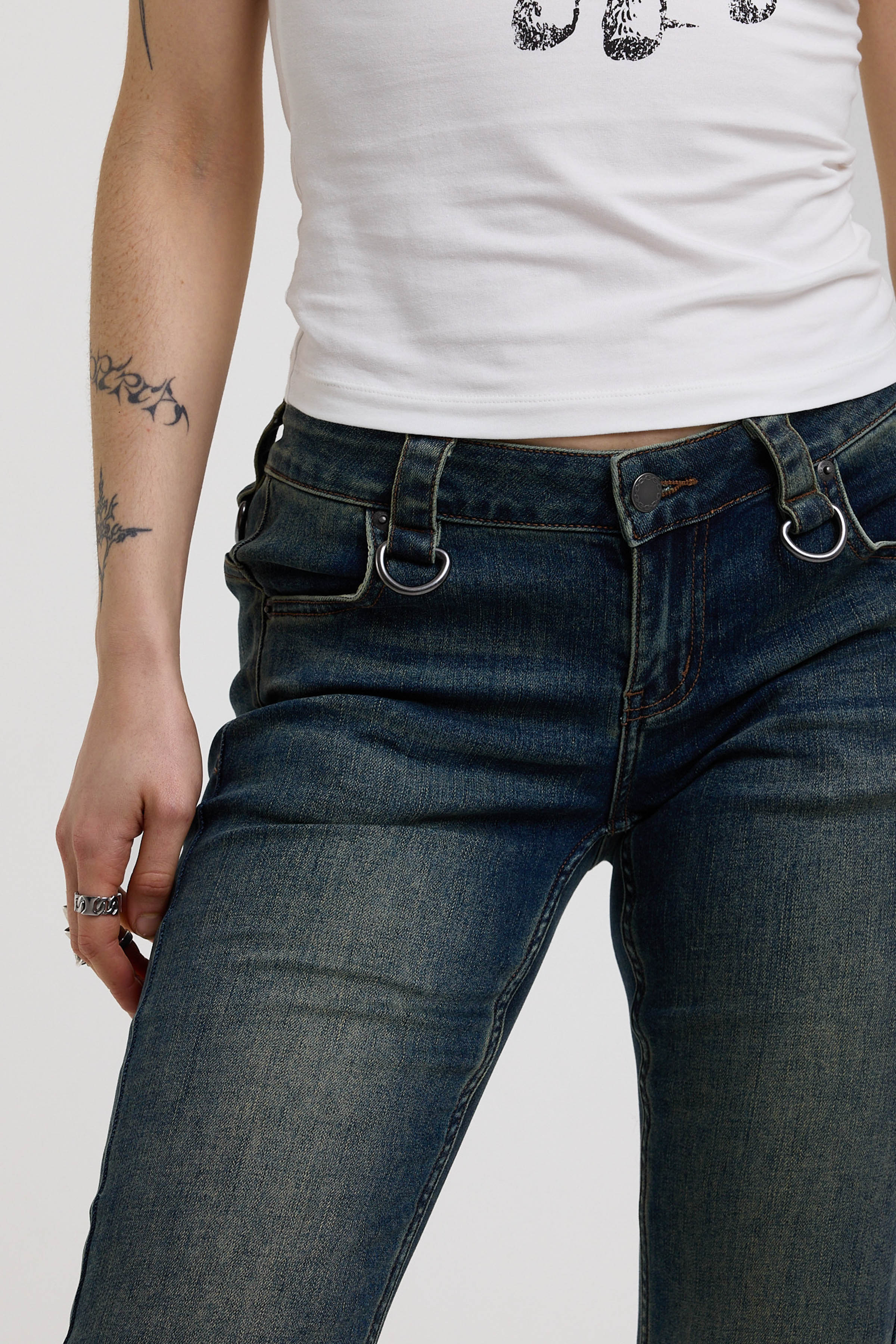 Close up of silver D-ring hardware detail at waistband on dark blue flare bootcut jeans, worn by model