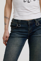 Close up of silver D-ring hardware detail at waistband on dark blue flare bootcut jeans, worn by model