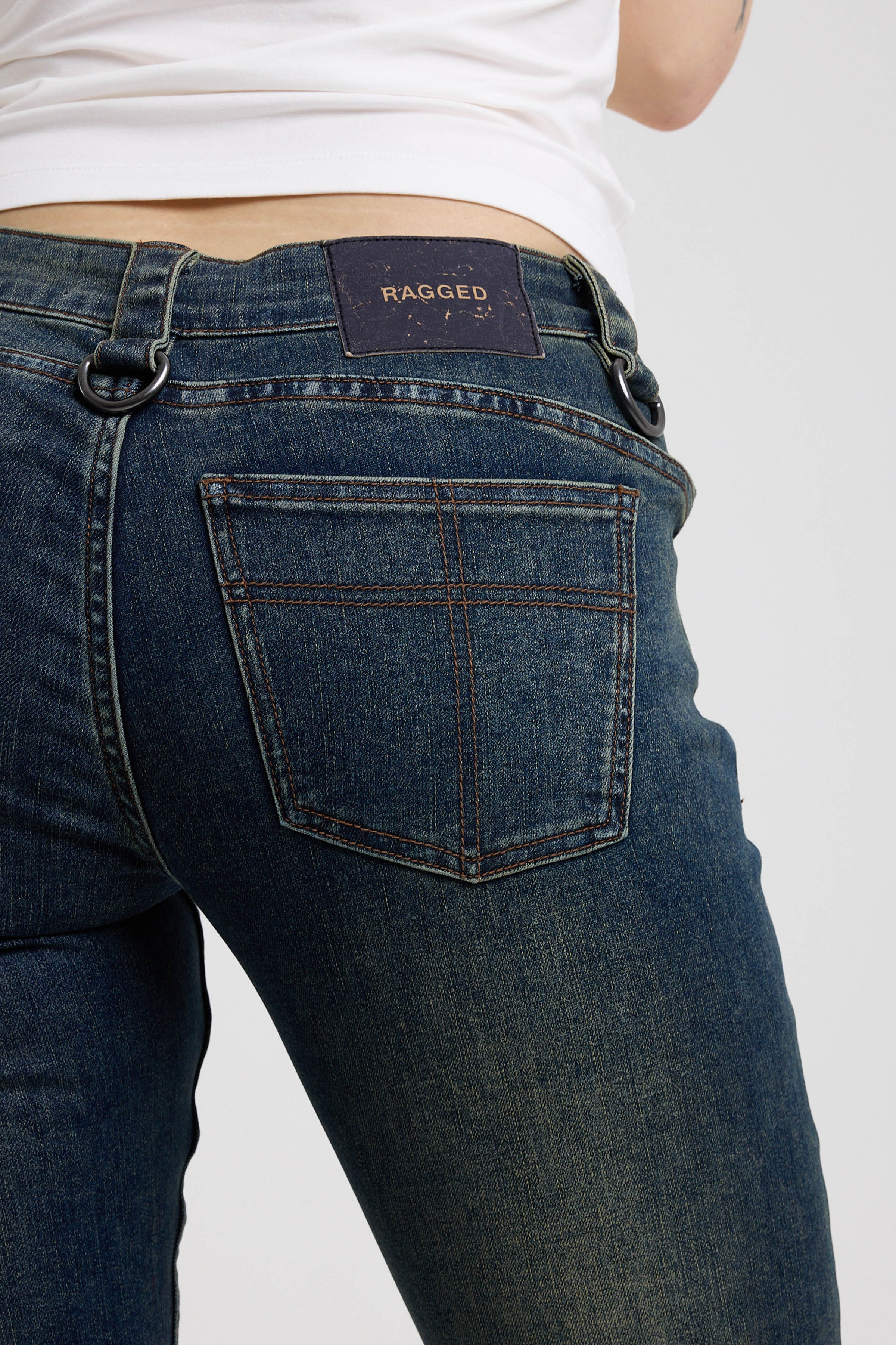 Close up of pocket with cross stitch and vegan leather tab on dark blue flare bootcut jeans with silver D-ring hardware detail, worn by model
