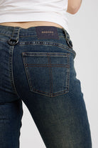 Close up of pocket with cross stitch and vegan leather tab on dark blue flare bootcut jeans with silver D-ring hardware detail, worn by model