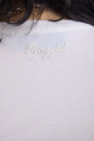 Close up of embroidered Ragged logo on white shrunken baby t-shirt, worn by a model