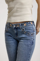 Detail showing eyelet and rivet cut outs on waistband of Blue flare bootcut jeans, worn by model