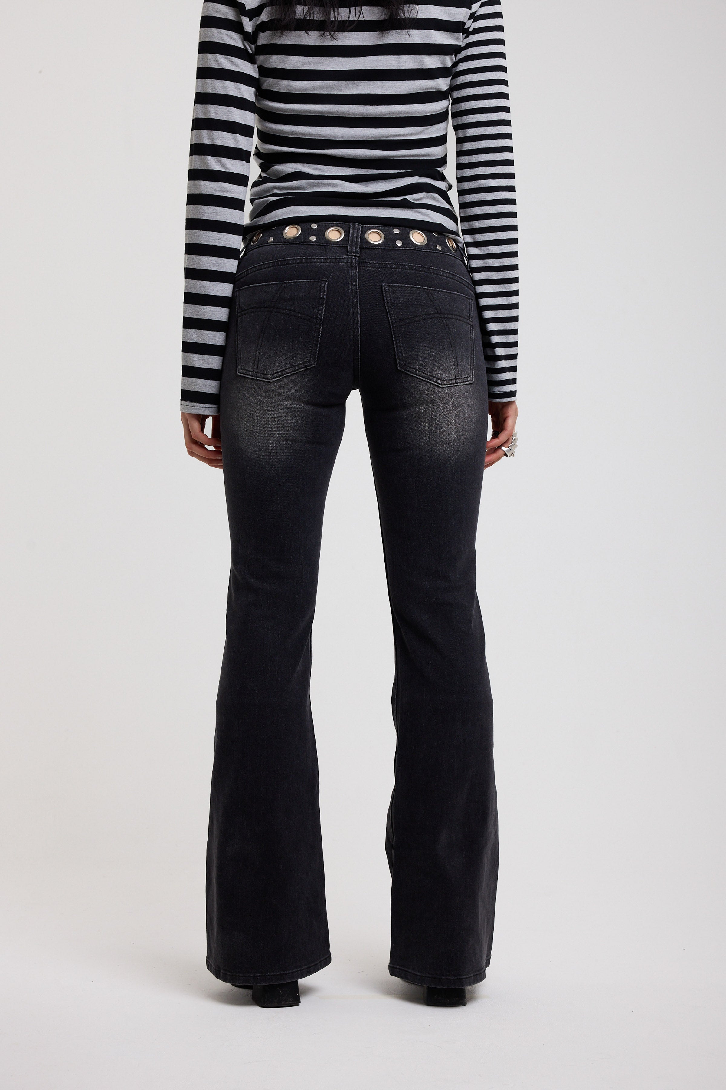 Back image of washed black flare bootcut jeans with eyelet cut out detail, worn by model