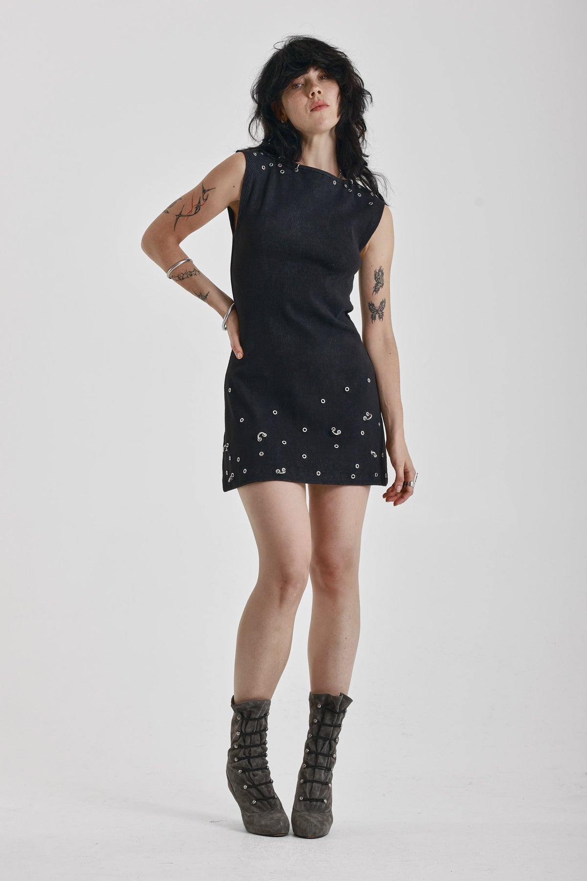 Black ribbed mini dress with slash neck and piercing and stud hardware details, worn by a model