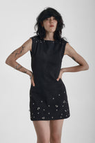 Black ribbed mini dress with slash neck and piercing and stud hardware details, worn by a model