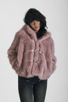 Dusty pink faux fur jacket with silver buckle clasps and a hood, worn by model