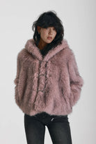 Dusty pink faux fur jacket with silver buckle clasps and a hood, worn by model