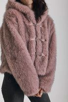 Dusty pink faux fur jacket with silver buckle clasps and a hood, worn by model