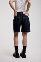 Back view of dark rinse denim jorts with seam detail and exposed zip, worn by model
