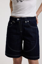 Dark rinse denim jorts with seam detail and exposed zip, worn by model