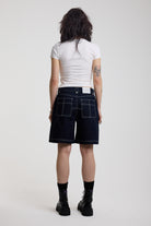 Back view of dark rinse denim jorts with seam detail and exposed zip, worn by model