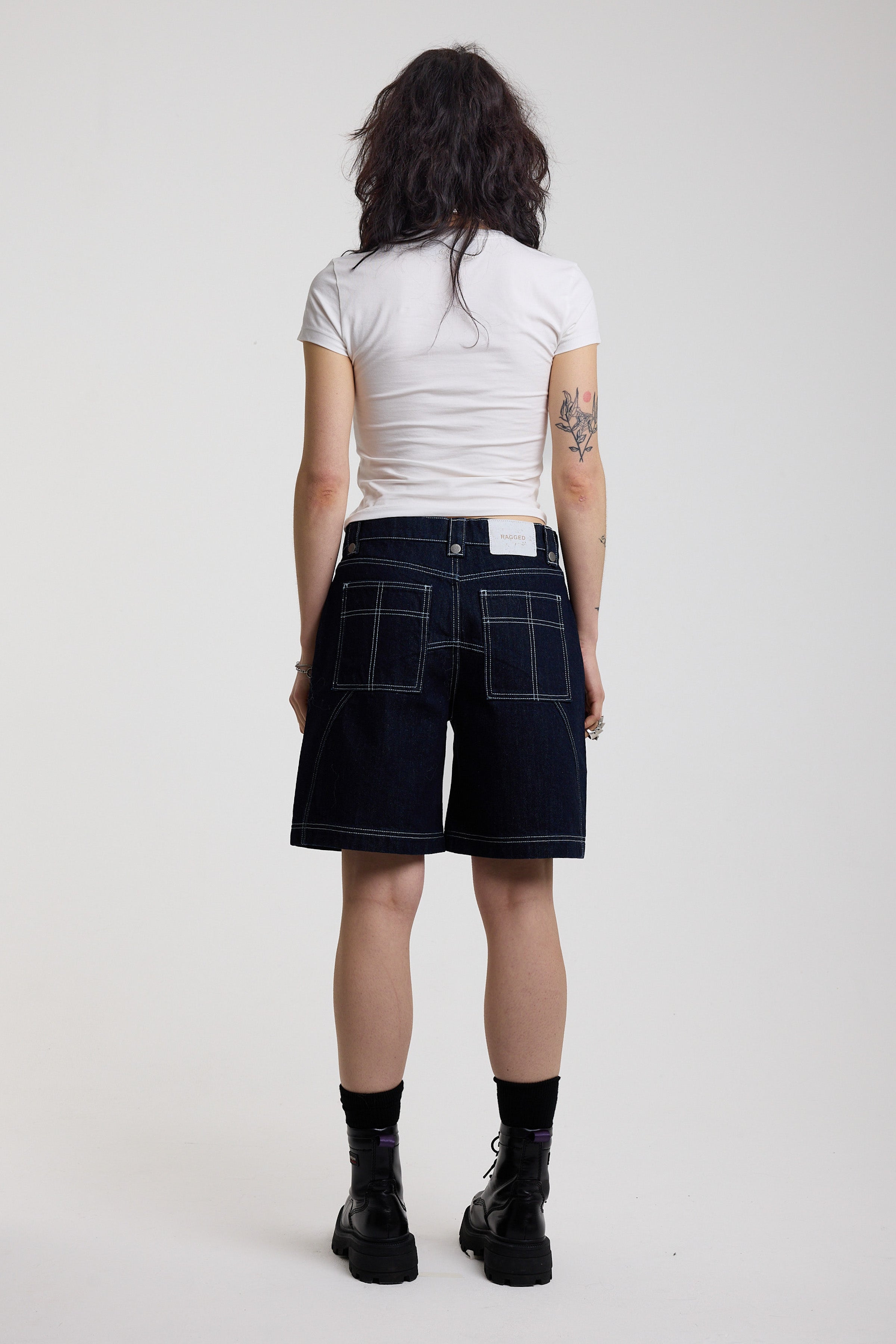 Back view of dark rinse denim jorts with seam detail and exposed zip, worn by model