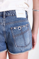 Mid blue denim mini shorts with raw hem and silver eyelet rivet and stud detail, worn by model