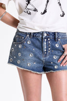 Mid blue denim mini shorts with raw hem and silver eyelet rivet and stud detail, worn by model