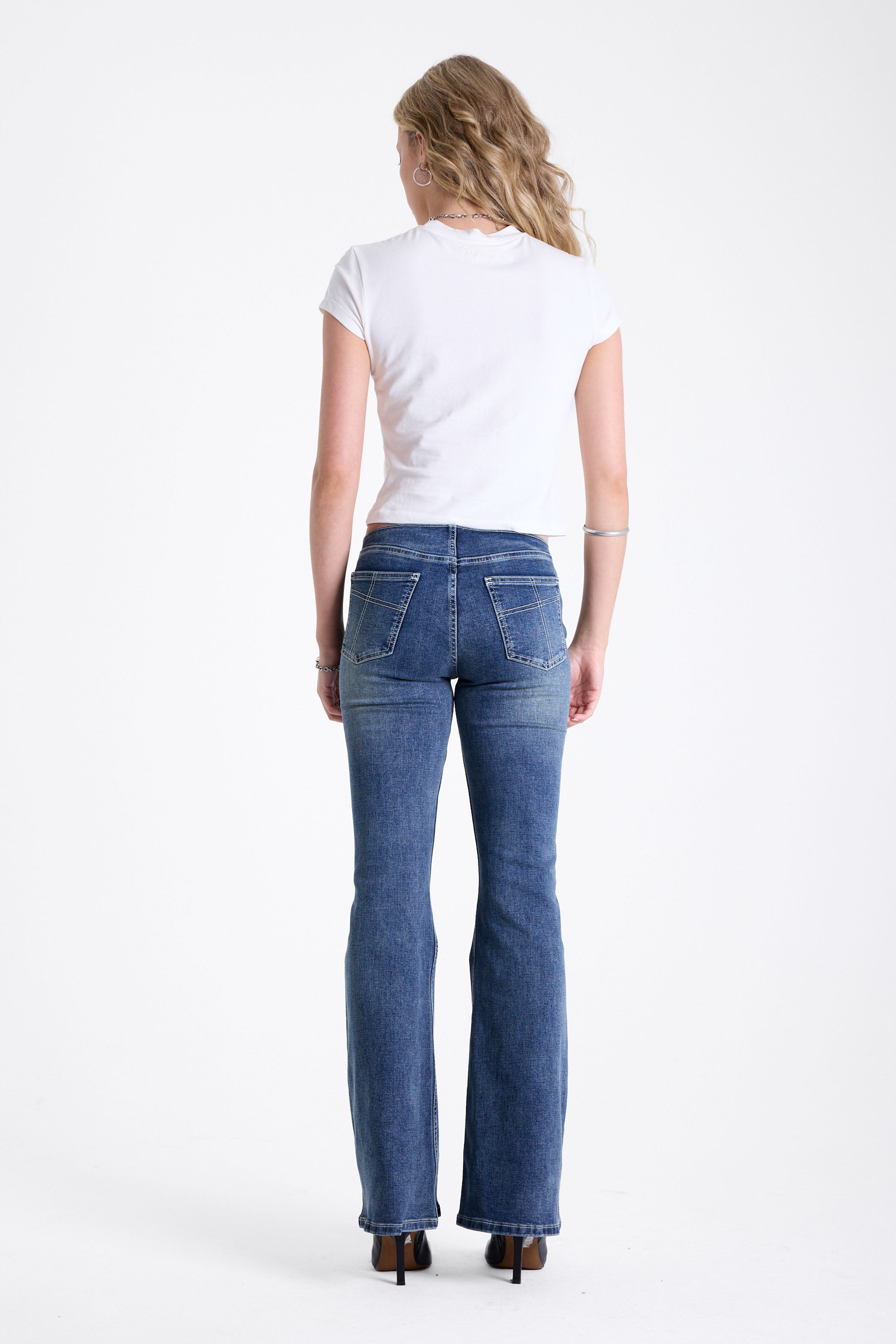 Mid blue denim flare jeans with silver latch buckle fastening and no waistband, worn by model.