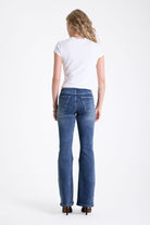 Mid blue denim flare jeans with silver latch buckle fastening and no waistband, worn by model.