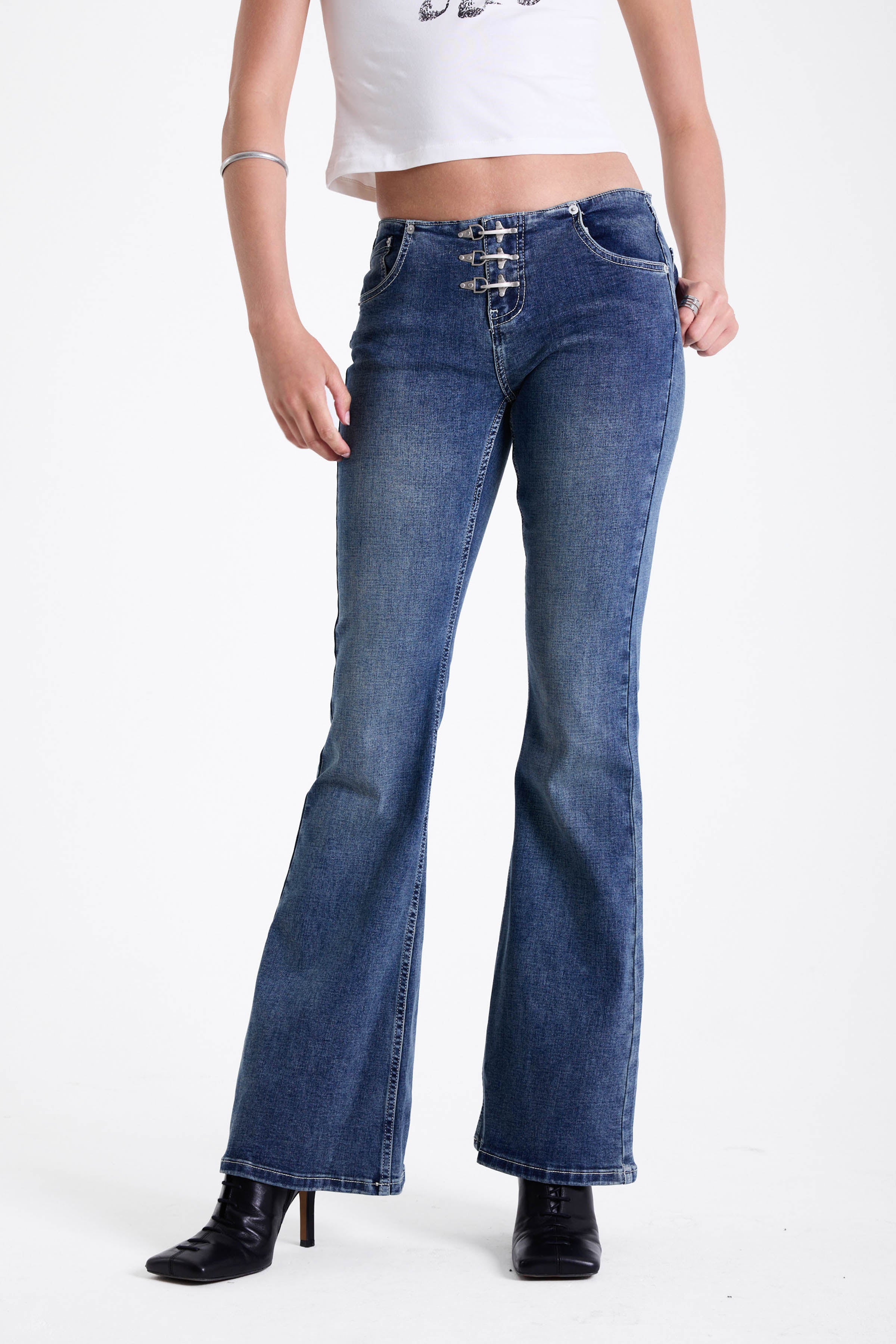 Mid blue denim flare jeans with silver latch buckle fastening and no waistband, worn by model.