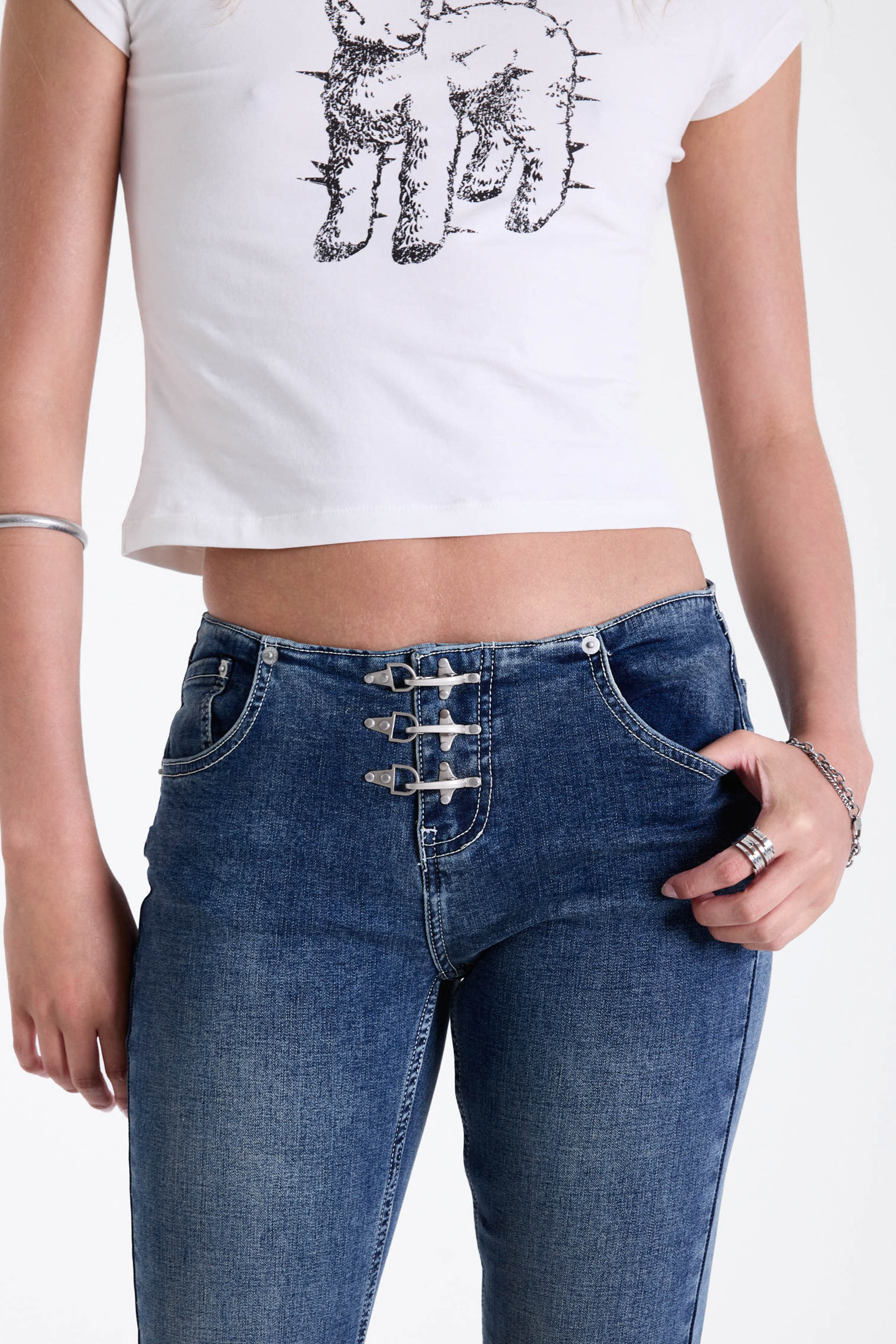 Mid blue denim flare jeans with silver latch buckle fastening and no waistband, worn by model.