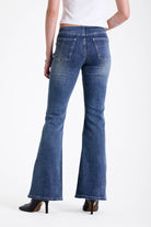 Mid blue denim flare jeans with silver latch buckle fastening and no waistband, worn by model.