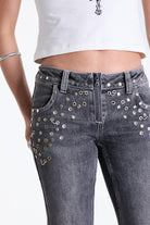 Washed grey low rise flare jeans with exposed front zip and silver stud and piercing hardware, worn by model.