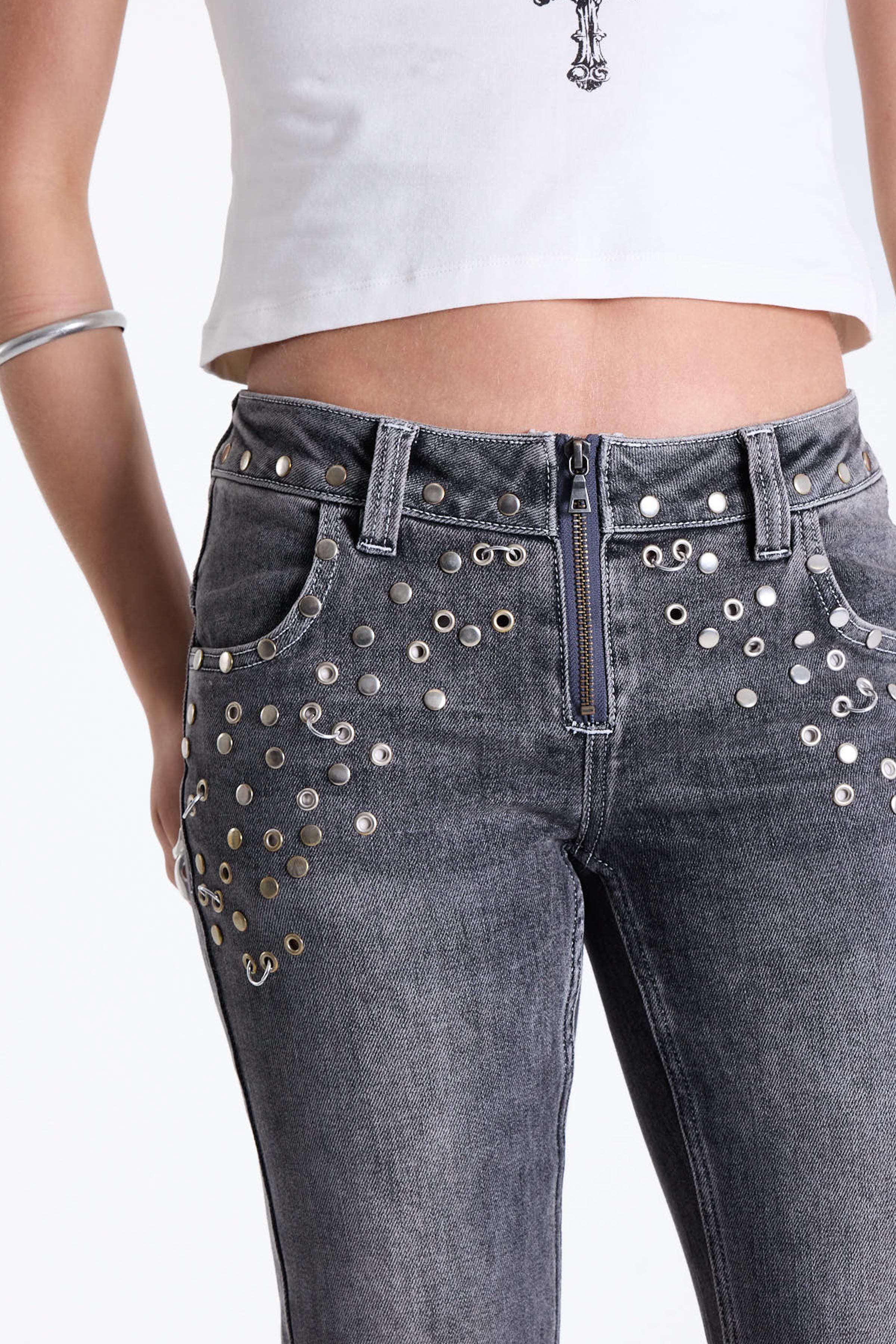 Washed grey low rise flare jeans with exposed front zip and silver stud and piercing hardware, worn by model.