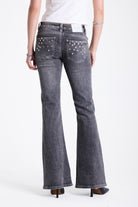 Washed grey low rise flare jeans with exposed front zip and silver stud and piercing hardware, worn by model.