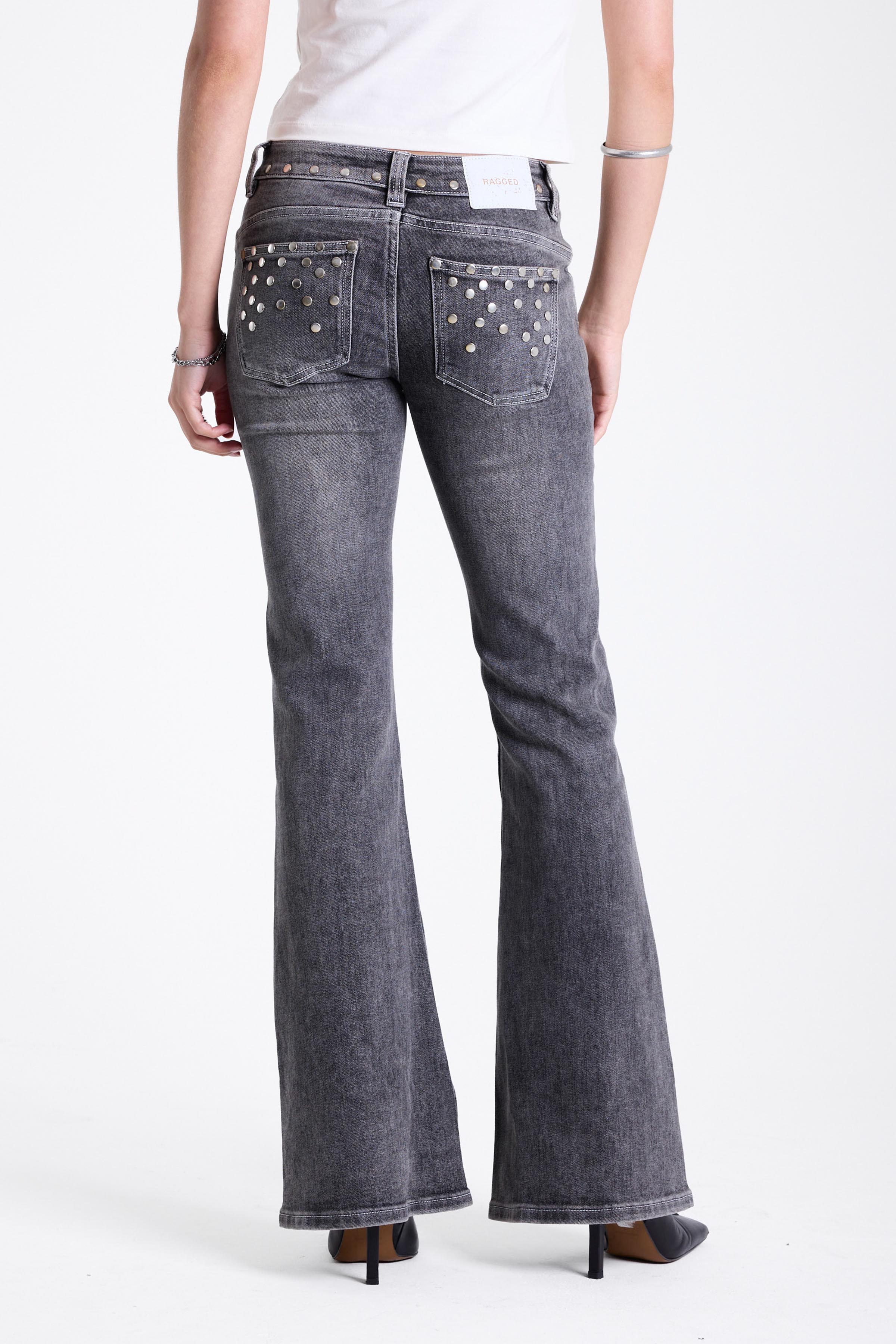 Washed grey low rise flare jeans with exposed front zip and silver stud and piercing hardware, worn by model.