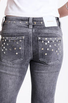 Washed grey low rise flare jeans with exposed front zip and silver stud and piercing hardware, worn by model.