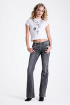 Washed grey low rise flare jeans with exposed front zip and silver stud and piercing hardware, worn by model.