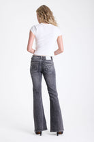 Washed grey low rise flare jeans with exposed front zip and silver stud and piercing hardware, worn by model.