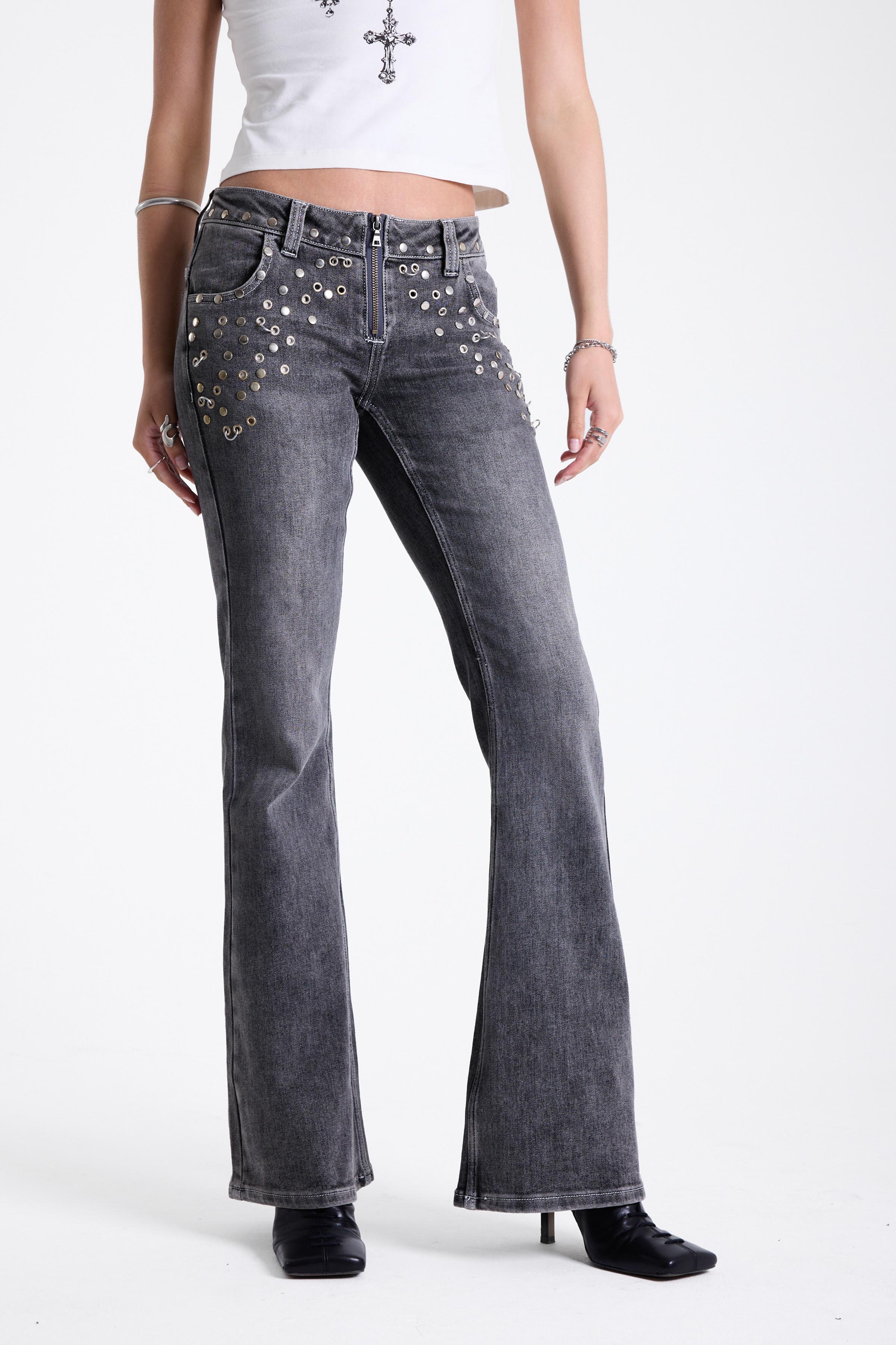 Washed grey low rise flare jeans with exposed front zip and silver stud and piercing hardware, worn by model.