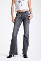 Washed grey low rise flare jeans with exposed front zip and silver stud and piercing hardware, worn by model.