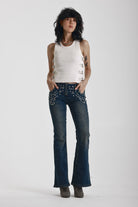 Indigo wash low rise flare jeans with exposed front zip and silver stud and piercing hardware, worn by model.