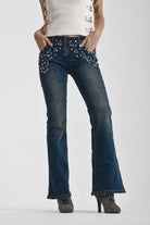 Indigo wash low rise flare jeans with exposed front zip and silver stud and piercing hardware, worn by model.
