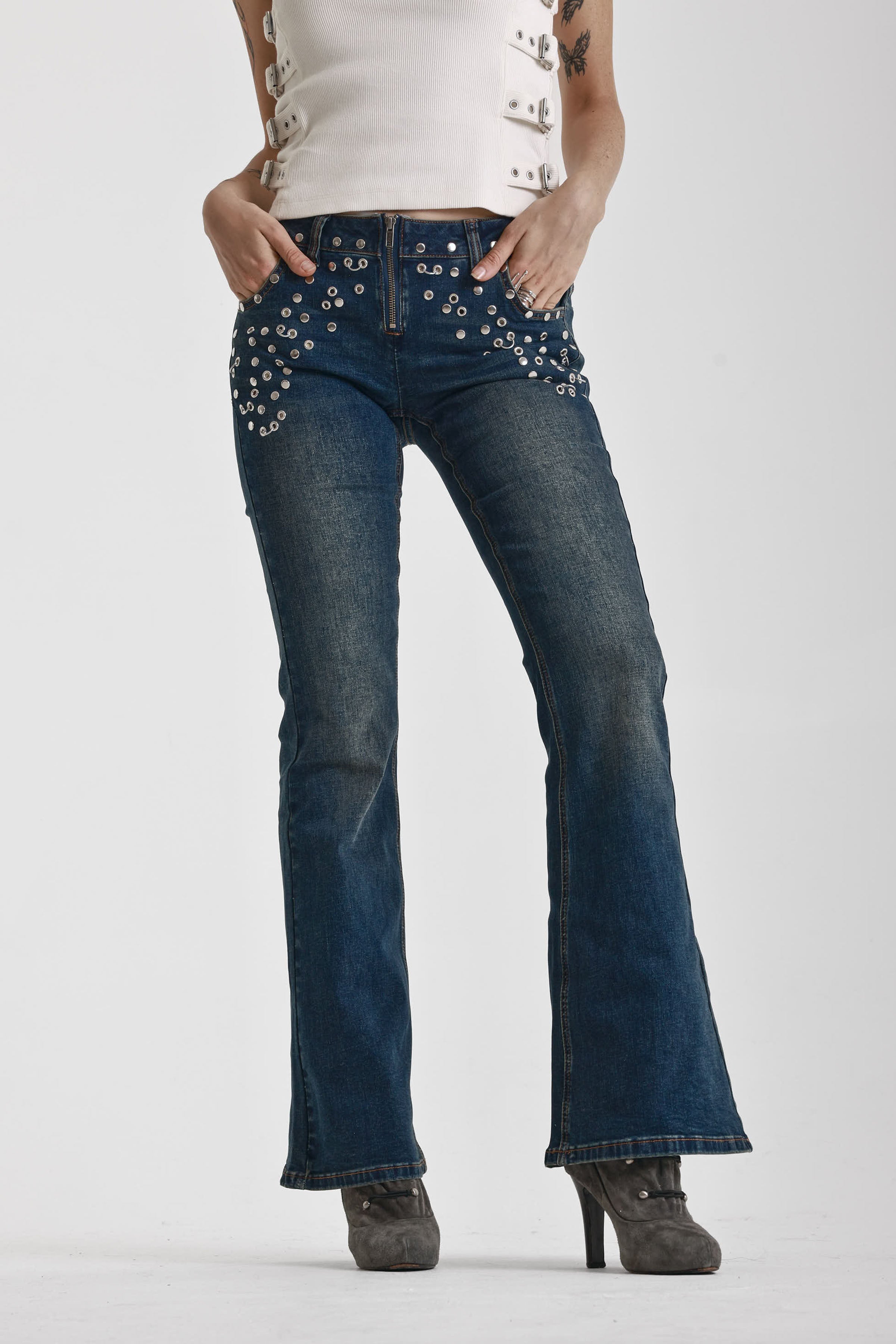 Indigo wash low rise flare jeans with exposed front zip and silver stud and piercing hardware, worn by model.