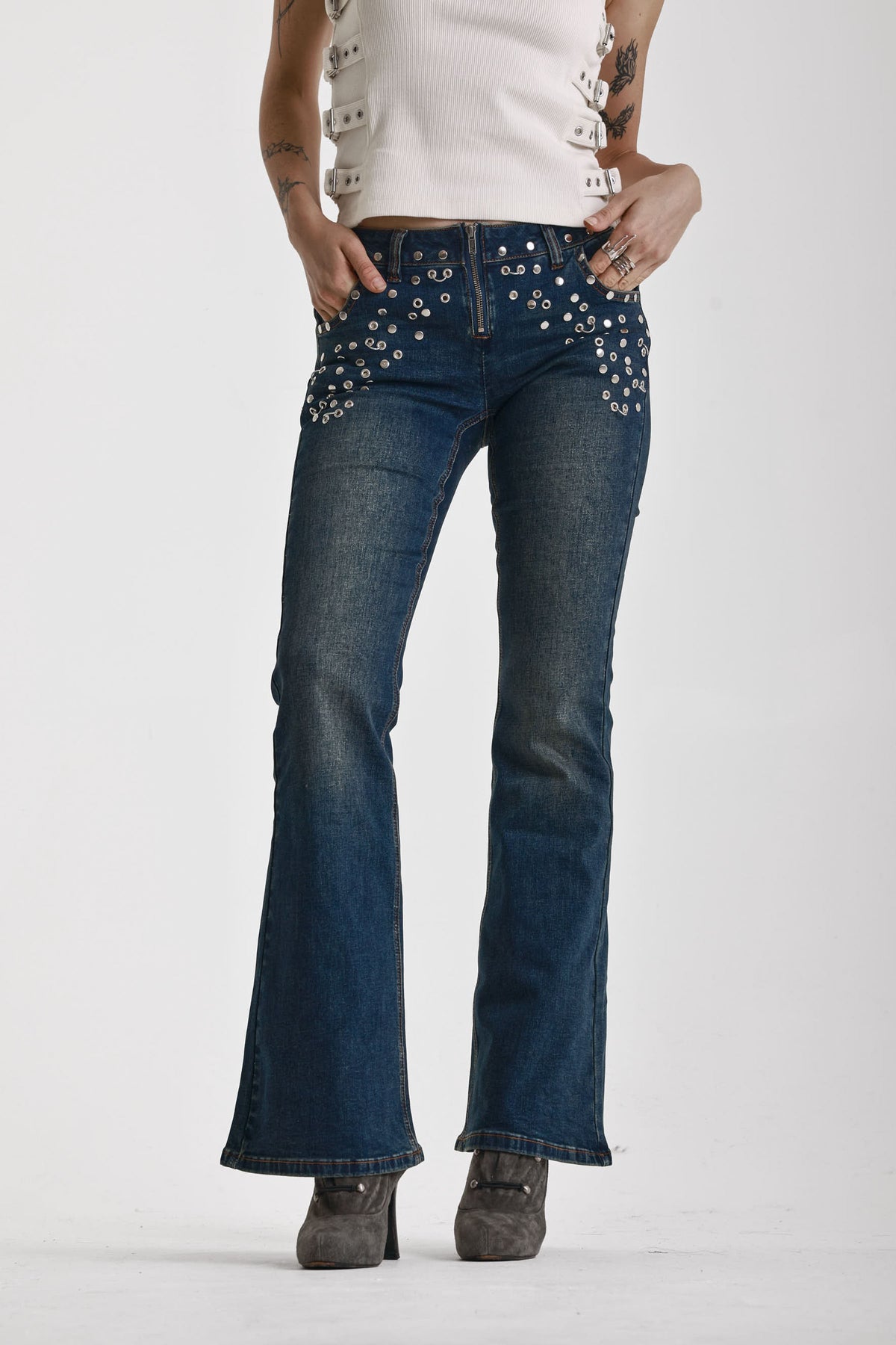 Indigo wash low rise flare jeans with exposed front zip and silver stud and piercing hardware, worn by model.