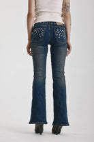 Indigo wash low rise flare jeans with exposed front zip and silver stud and piercing hardware, worn by model.