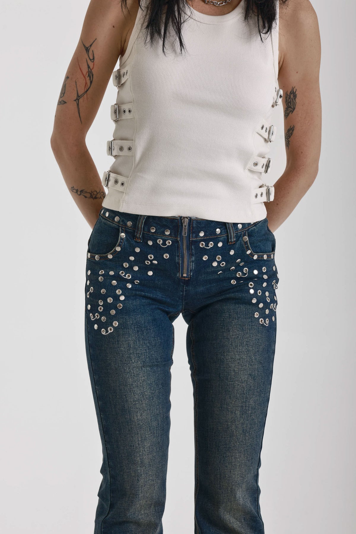 Indigo wash low rise flare jeans with exposed front zip and silver stud and piercing hardware, worn by model.
