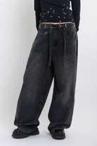 Washed black ultra baggy colossus jeans with silver eyelet waistband detail, worn by model 