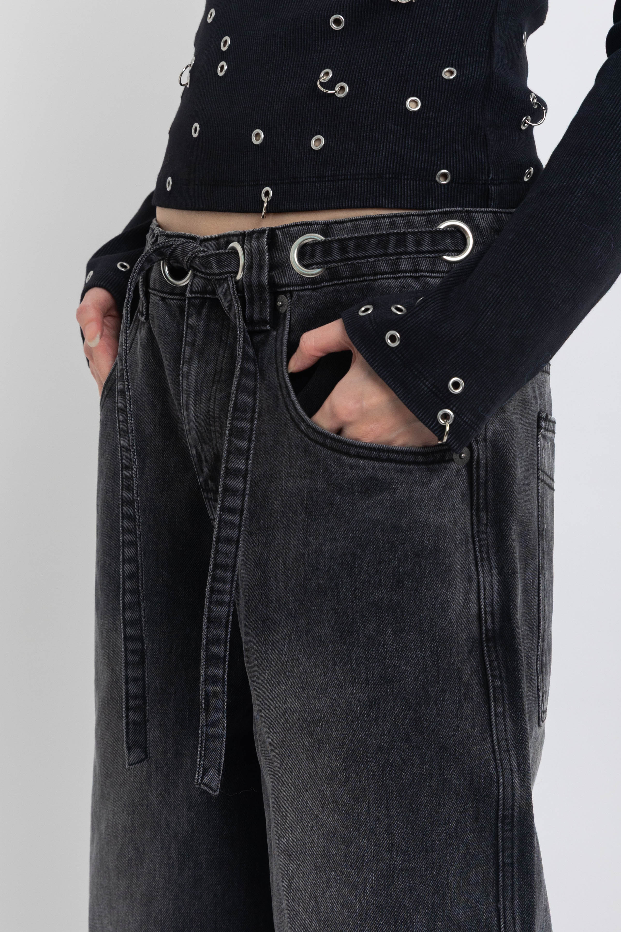Washed black ultra baggy colossus jeans with silver eyelet waistband detail, worn by model 