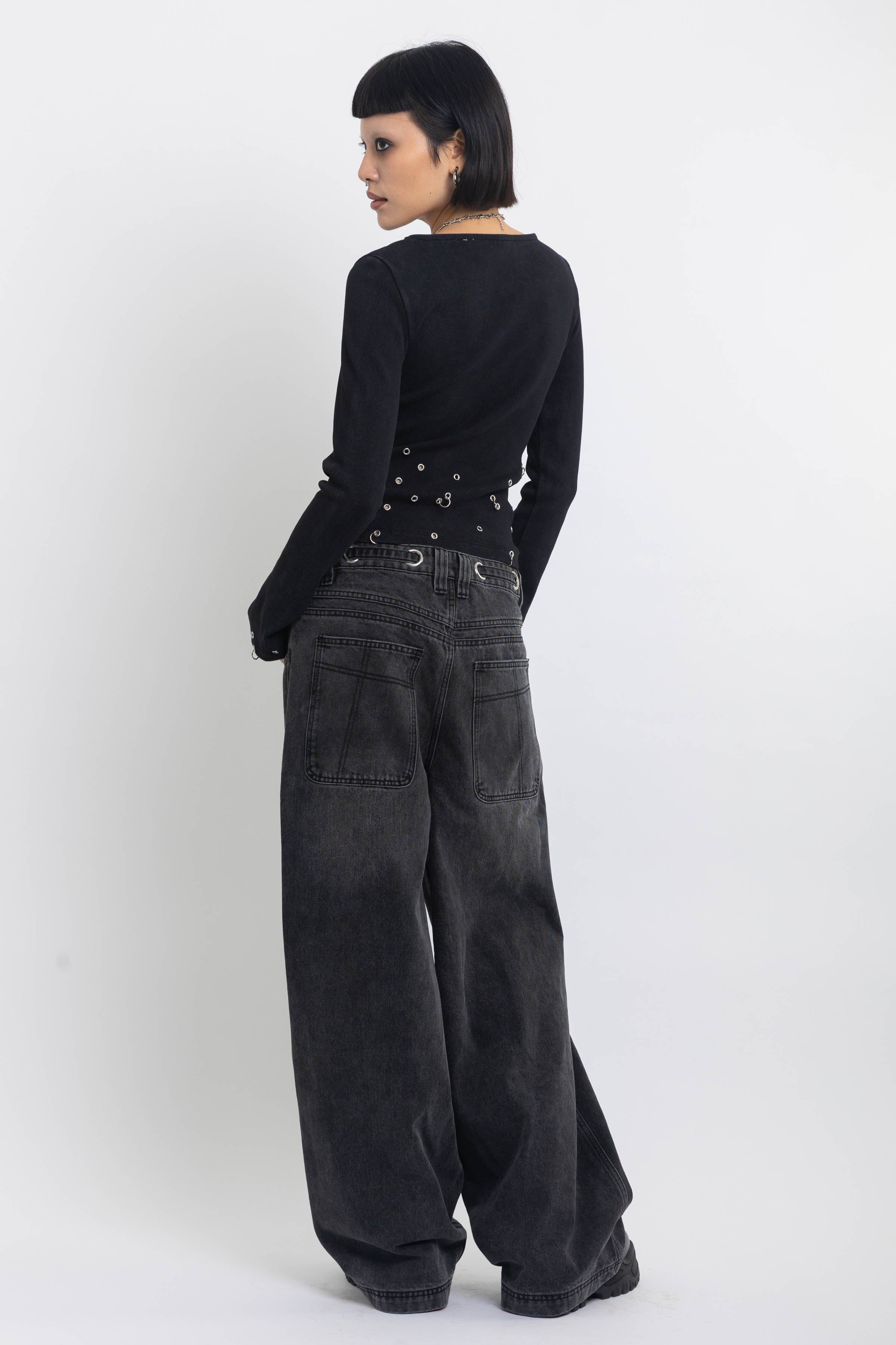Washed black ultra baggy colossus jeans with silver eyelet waistband detail, worn by model 