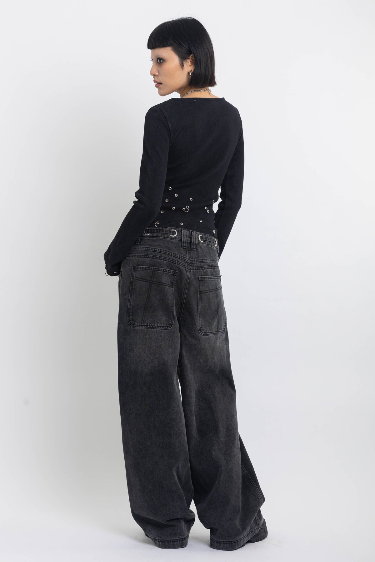 Washed black ultra baggy colossus jeans with silver eyelet waistband detail, worn by model 