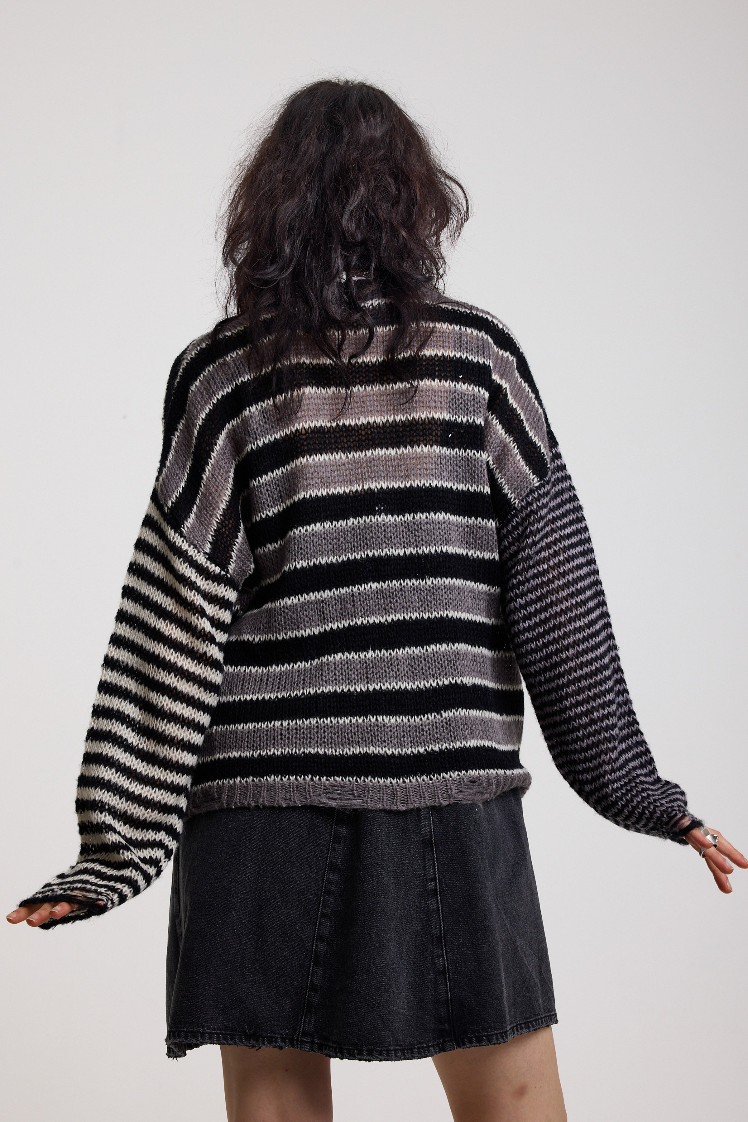 Back image of black and white stripe oversized knit jumper with grunge distressed details, worn by model