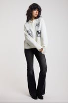 Cream oversized knit jumper with black graphic patch details and polo collar with black flare jeans, worn by model