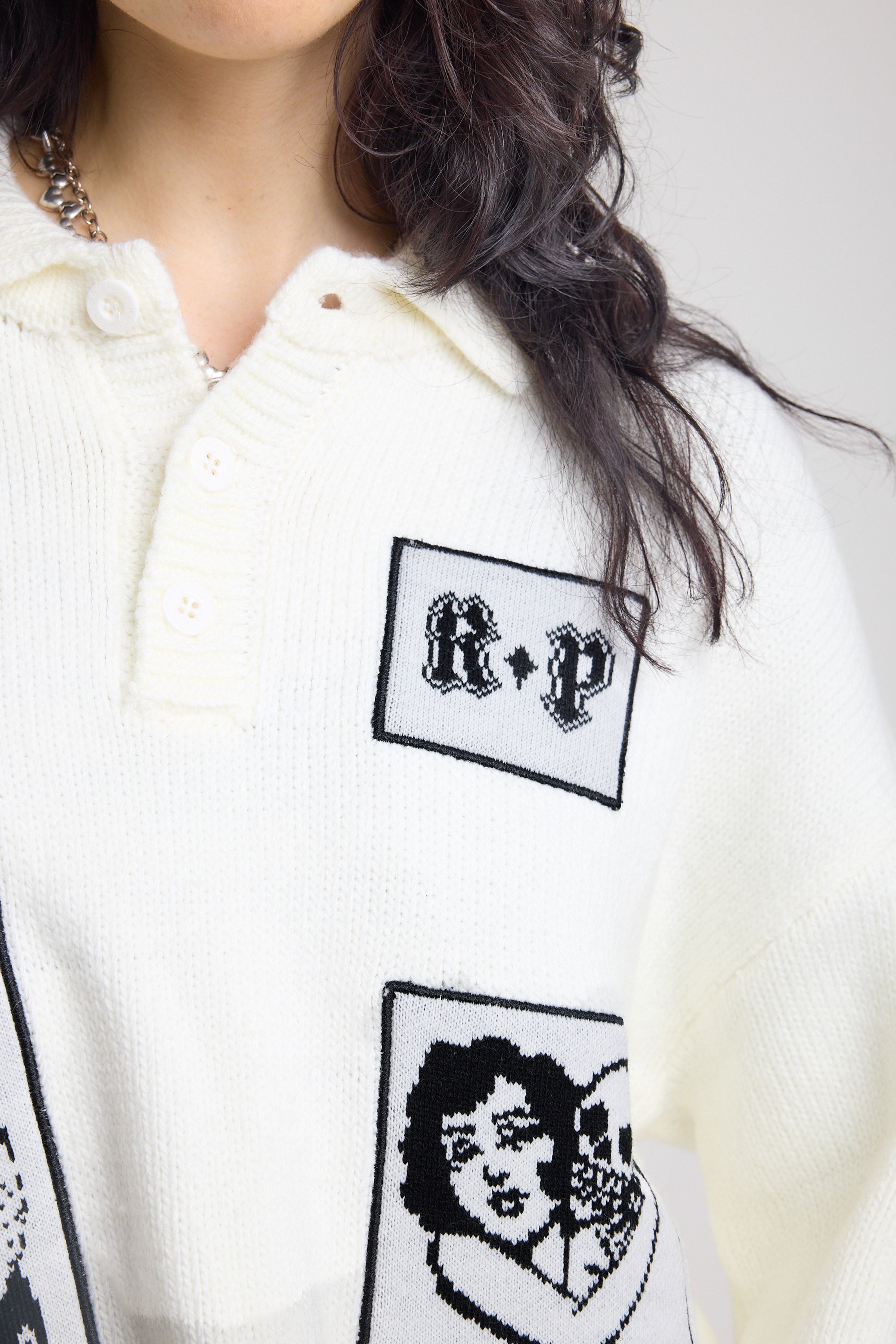 Close up of cream oversized knit jumper with black graphic patch details 