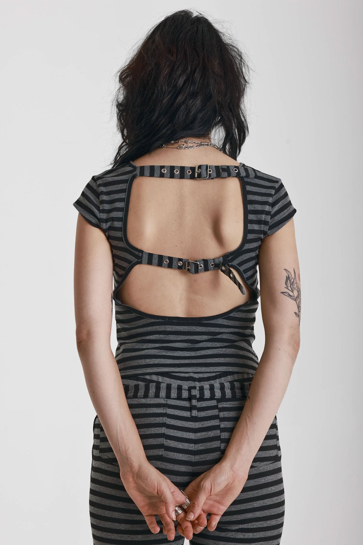 Grey and black stripe cap sleeve t-shirt with open back and eyelet buckle straps, worn by model